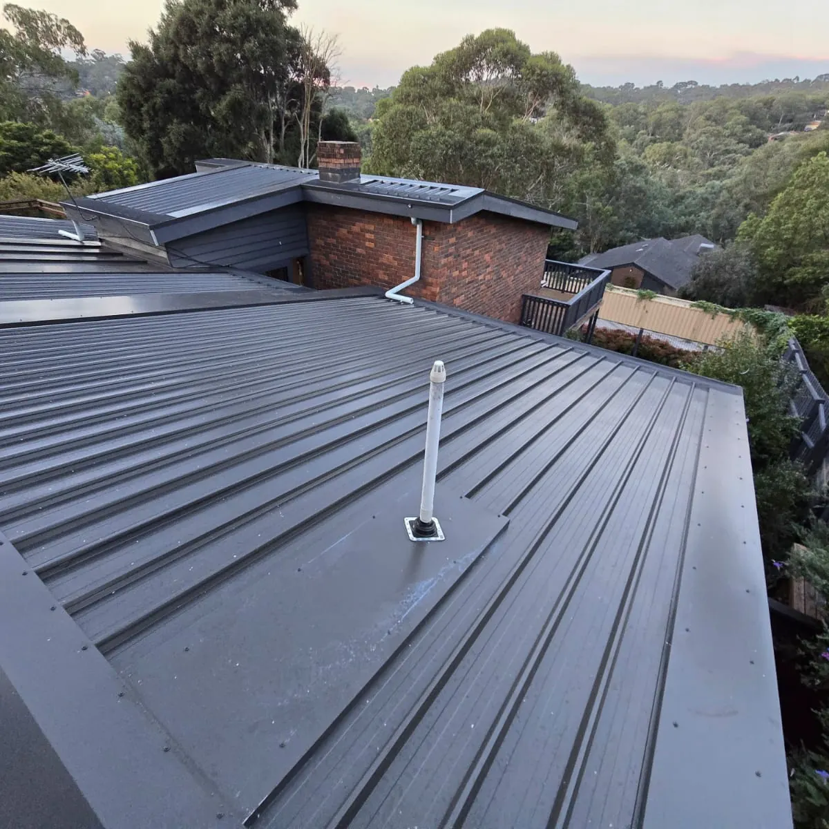 New charcoal metal roof flashed around a brick chimney