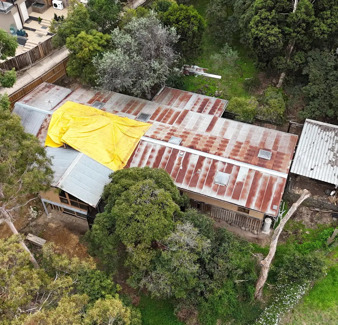 Rusted roof with a tarpaulin over a leak before replacement